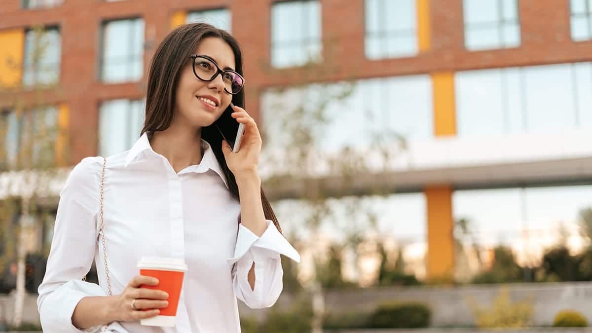 Woman wearing professional wardrobe talks on the phone outside.