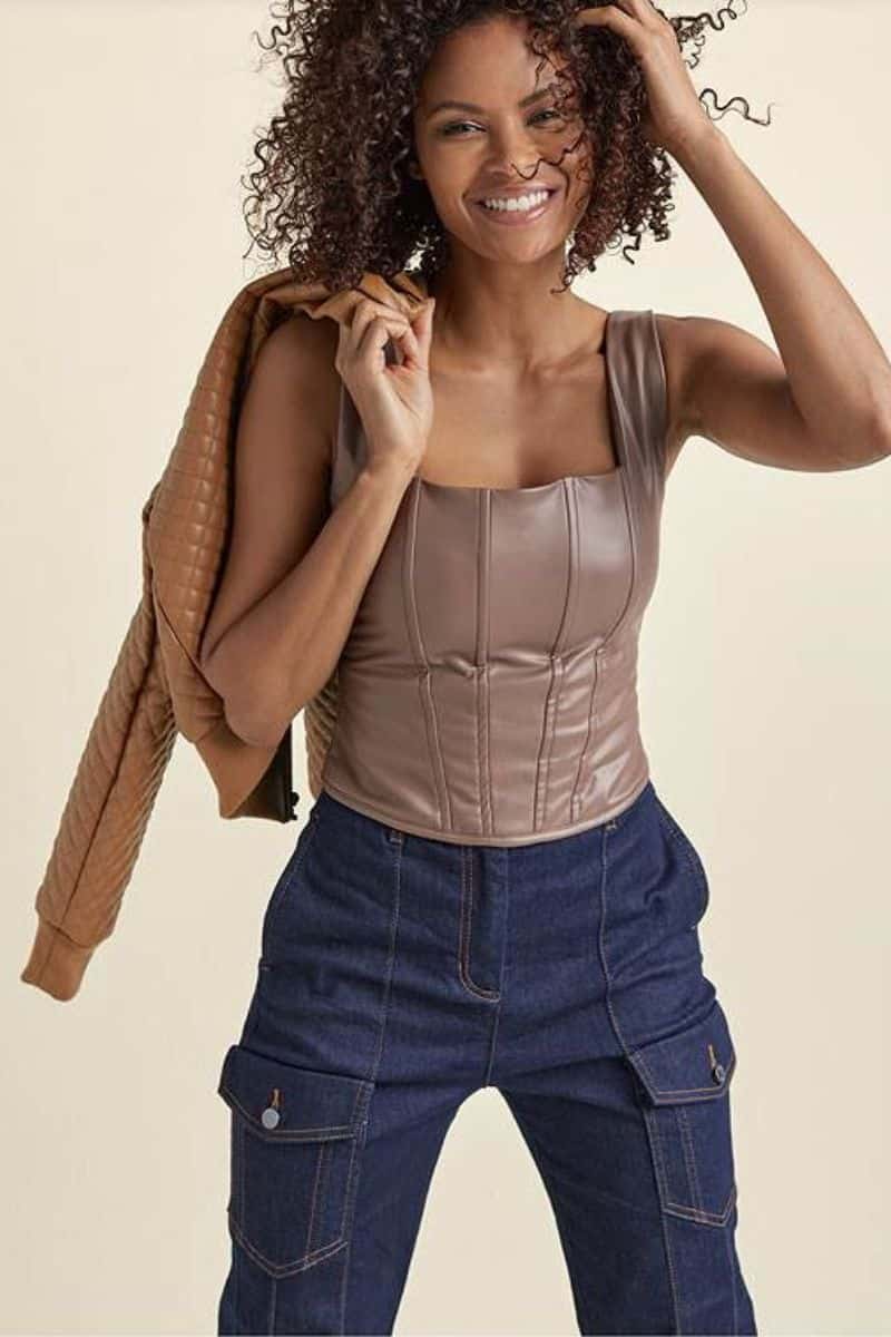 Leather Clothes are Trending: Here's How to Wear Them 8 Smiling model wears leather corset top with jeans.