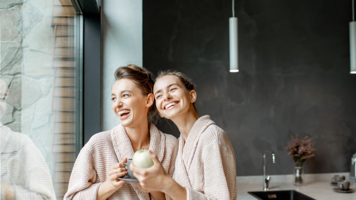 Two women wearing robes inside laughing.