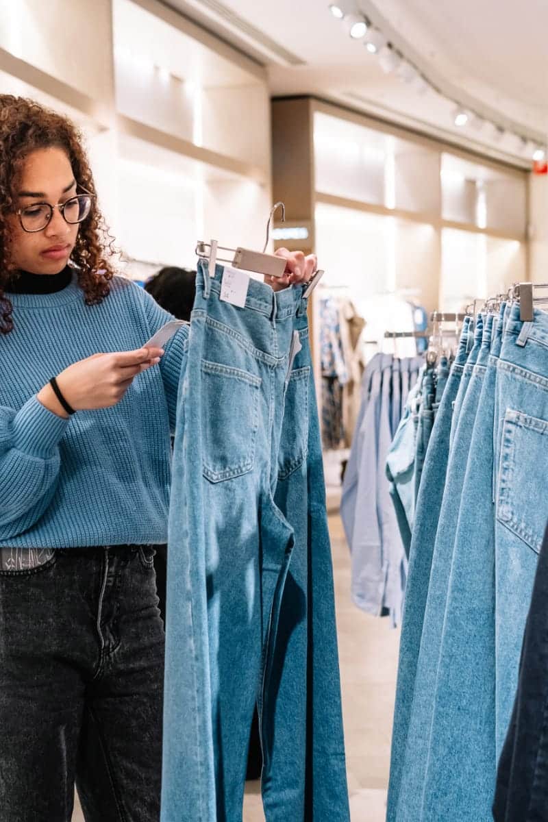 Cost Per Wear: How to Maximize Your Clothing Budget 1 Woman checks price tag of jeans to represent cost per wear concept.