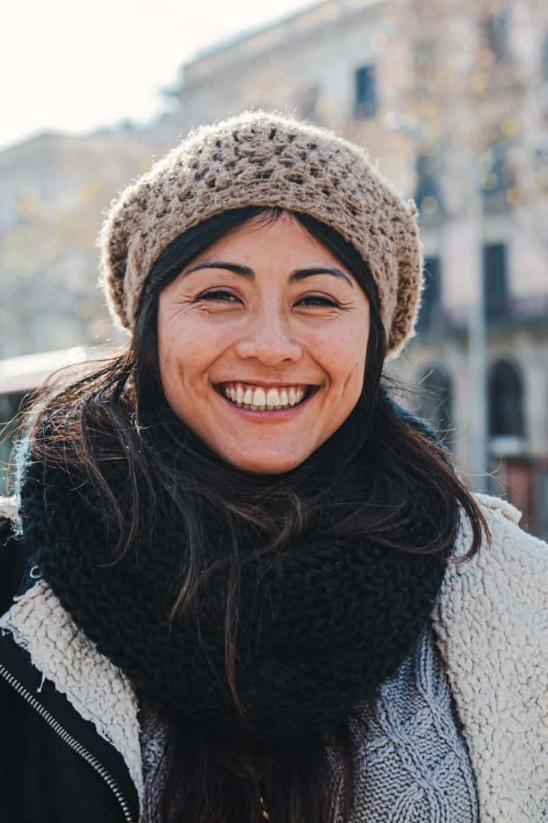 What to Wear While Traveling for the Holidays 1 Smiling woman wearing beanie and sweater to demonstrate what to wear while traveling.