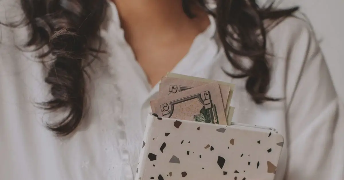 How Do Clothes Fit in the 50/30/20 Budget? 13 Close-up of woman holding folder with cash sticking out of it.