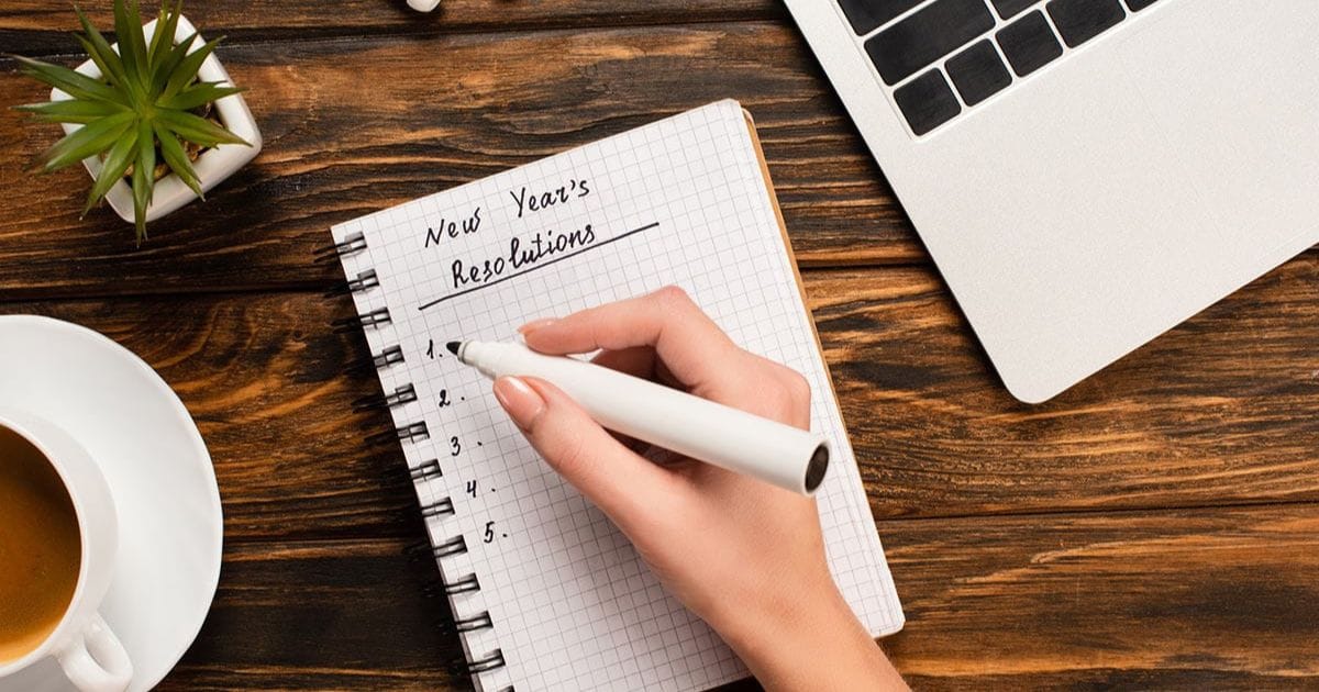 6 New Year's Resolutions for 2024 and the Tools You Need to Keep Them 57 Close view of hand writing out New Year's resolutions in a spiral bound book.