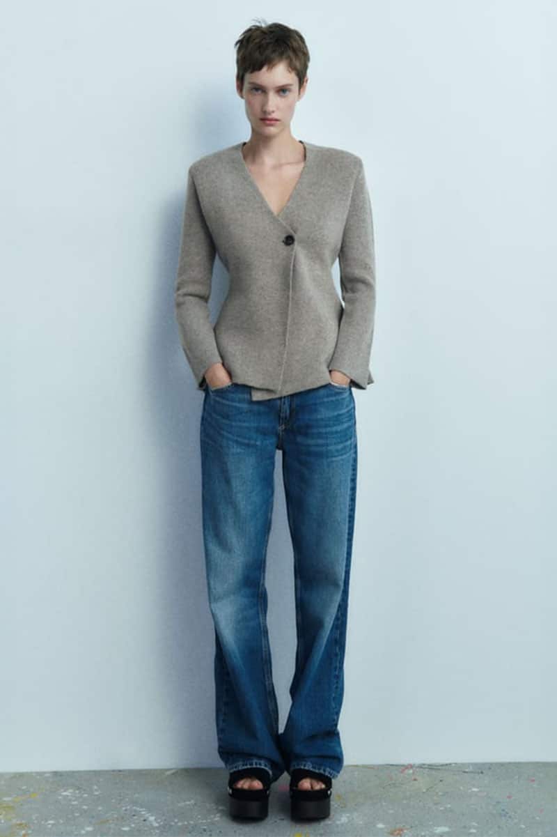 Model wears peplum jacket in front of a gray background. 