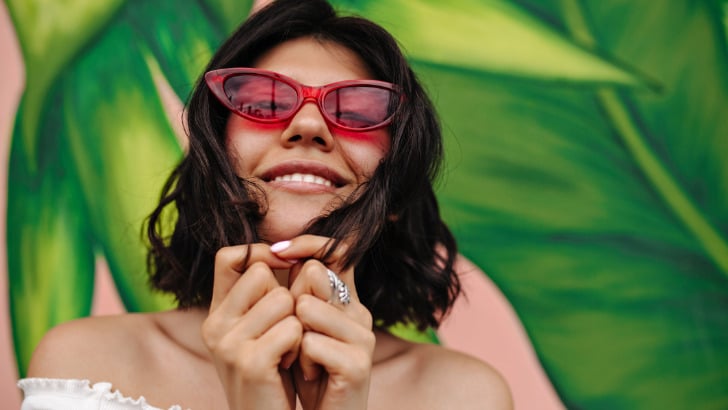 What Kind of Sunglasses to Buy 92 Woman smiles while wearing pink cat-eye sunglasses.
