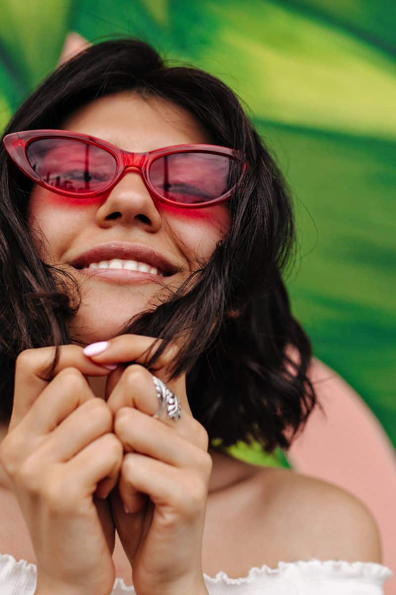What Kind of Sunglasses to Buy 1 Woman smiles while wearing pink cat-eye sunglasses.