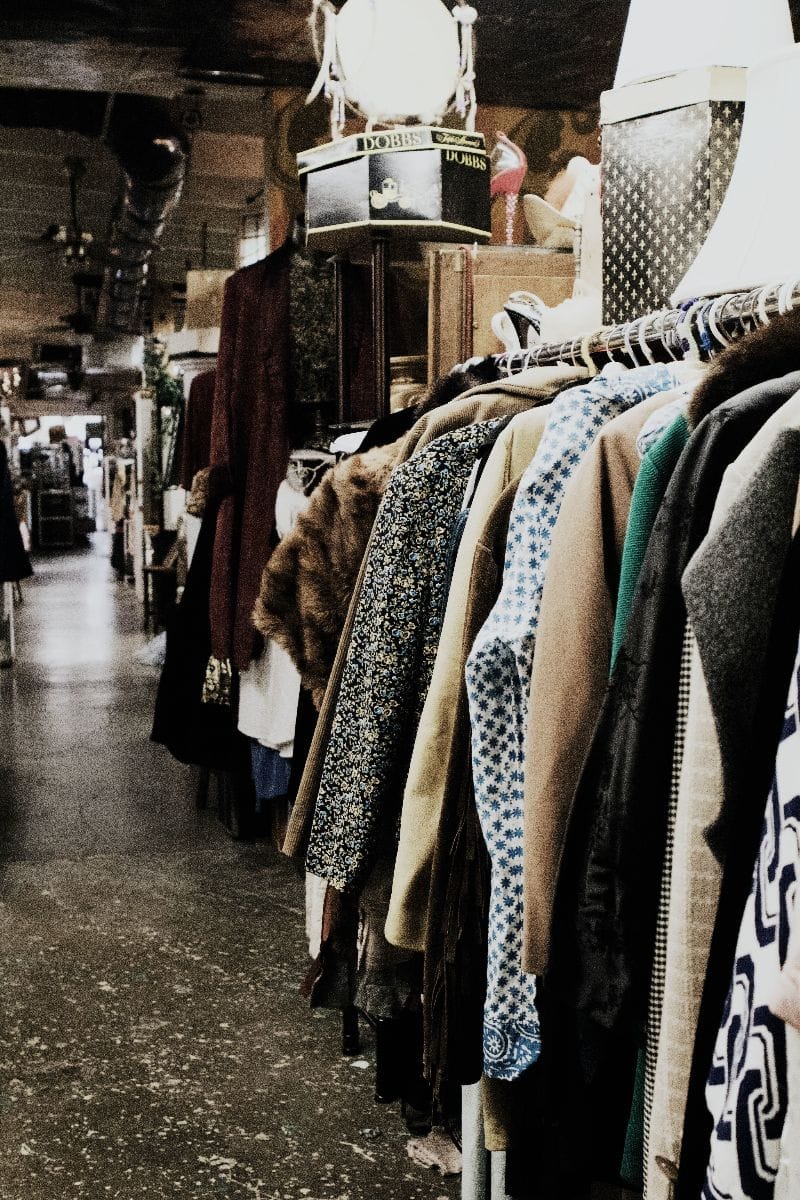 What to Buy at Thrift Stores: 5 Product Categories to Shop Secondhand 2 Clothing hanging on rack in thrift store.