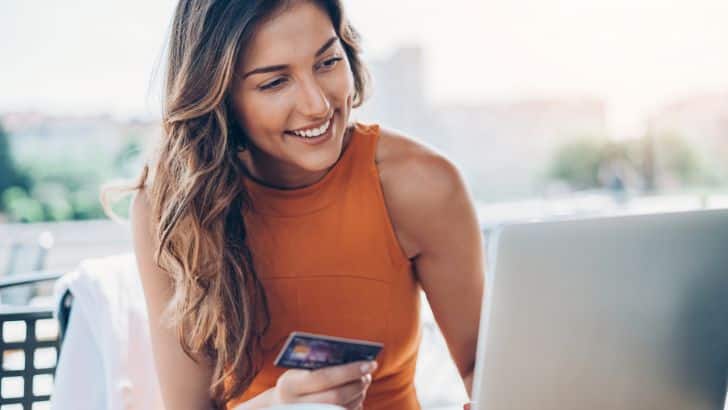 Farfetch Sale: 10 Designer Pieces to Shop Now for Less 88 Woman shops Farfetch sale on her laptop.