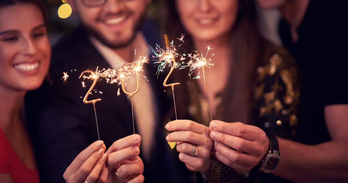 8 Essentials for a Stylish New Year's Eve Party 60 Smiling adults hold up candles shaped like 2024 during New Year's Eve party.