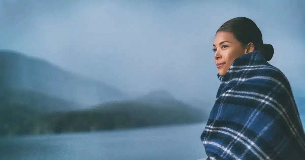 3 Dry Skin Myths That Could Spoil Your Next Vacation 47 Woman standing on cruise ship deck wrapped in blanket to represent dry skin and travel.