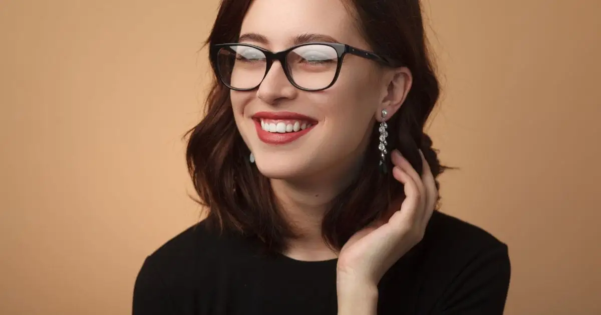 Should You Go Cheap on Eyeglass Frames? 41 Smiling woman wears eyeglasses in front of tan background.