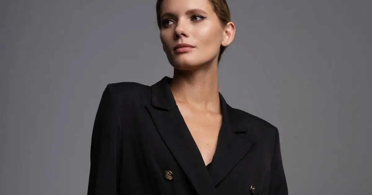 The 7 Fashion Essentials Women 40+ Need in 2024 40 Woman wearing black blazer against gray background.